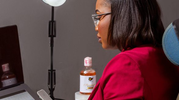 A woman in an office setting working on a laptop with skincare products beside her.